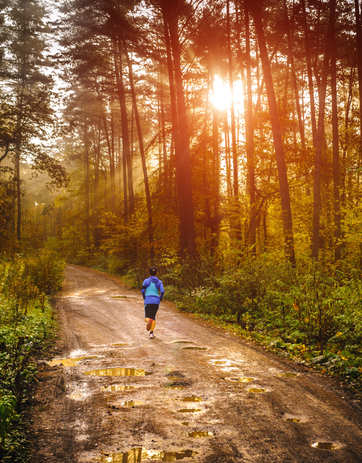 Een hardloper rent over een modderig bospad tijdens de opkomende zon